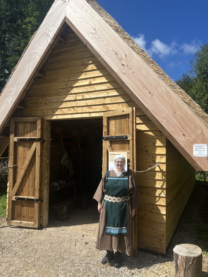 A member of staff at WWT Martin Mere is dressed as a Viking. They are stood in front of the Longhouse at Mere Tun.